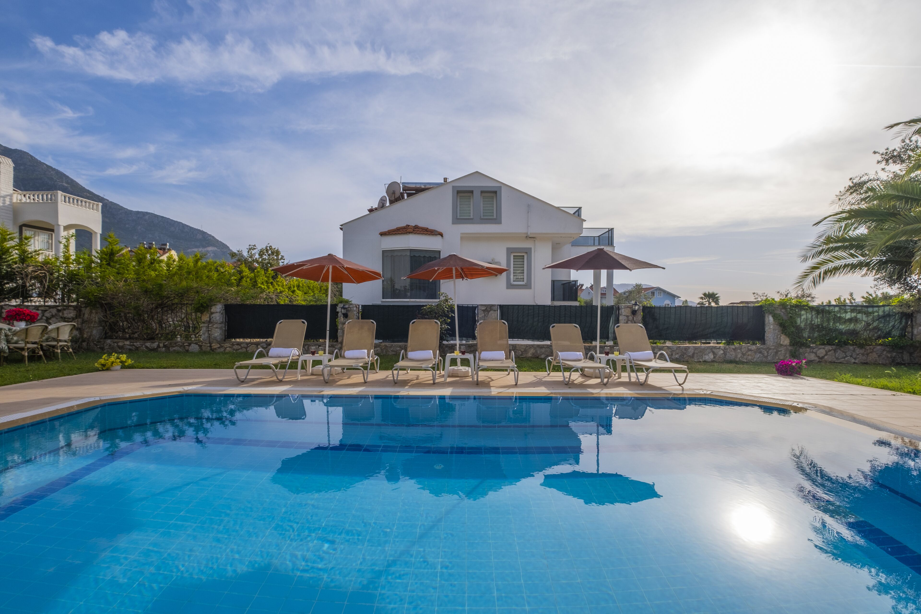 Ein Swimmingpool mit Liegestühlen und Sonnenschirmen, umgeben von einem Haus und Grünflächen.