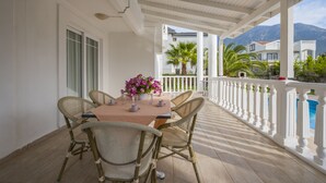 A covered outdoor dining area with a table and chairs, a potted plant, and a view of a mountain and pool. - Infinity Civan Villa (Fethiye)
