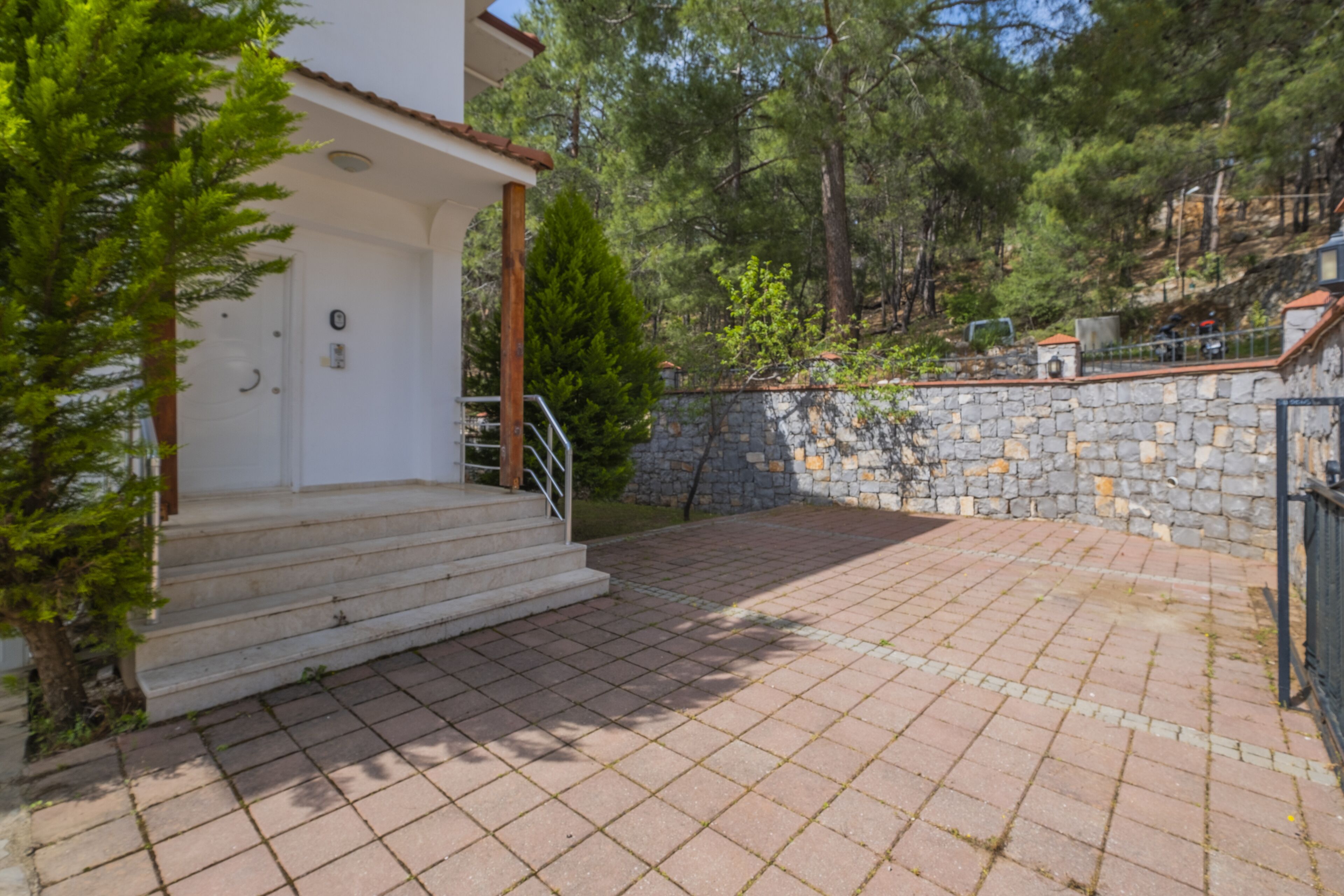 Un patio empedrado con muros de piedra y una escalera de madera que conduce a un edificio blanco con una puerta y un pequeño porche.
