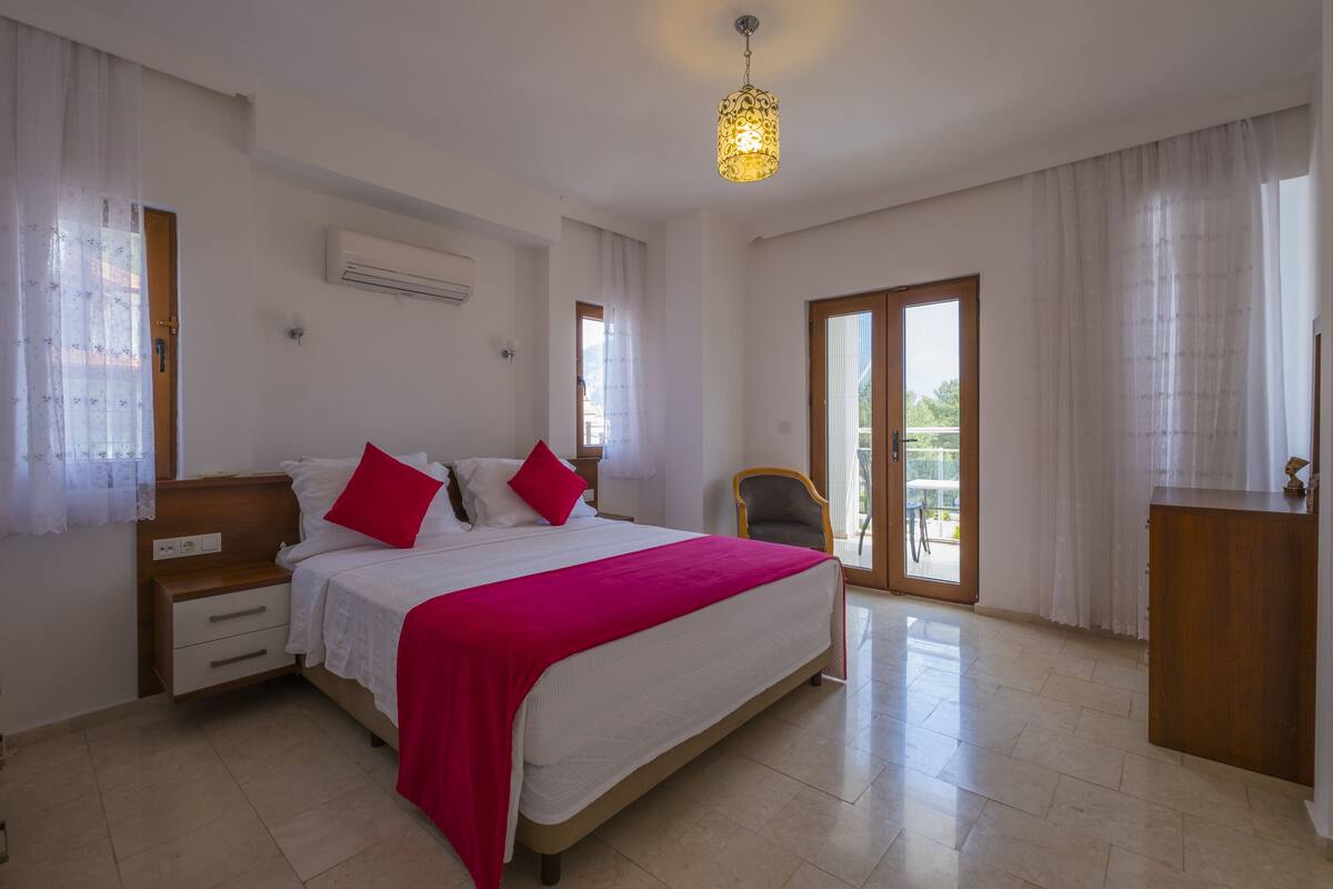 A spacious bedroom with a large bed, a wooden nightstand, a desk, and a chair.