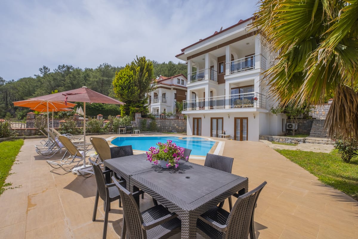 A poolside area with a dining table and chairs, a pool, and a multi-story building with balconies.