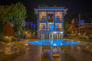 A two-story building with a swimming pool, outdoor seating, and a well-lit balcony. - Infinity Olympia Villas (Fethiye)