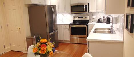 A modern kitchen with white cabinets, stainless steel appliances, and a glass dining table with a vase of flowers.