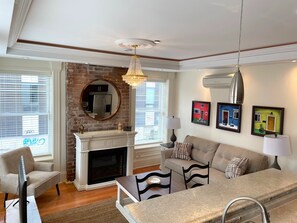 Una sala de estar con chimenea, un conjunto de sofás, una mesa de comedor y una araña.