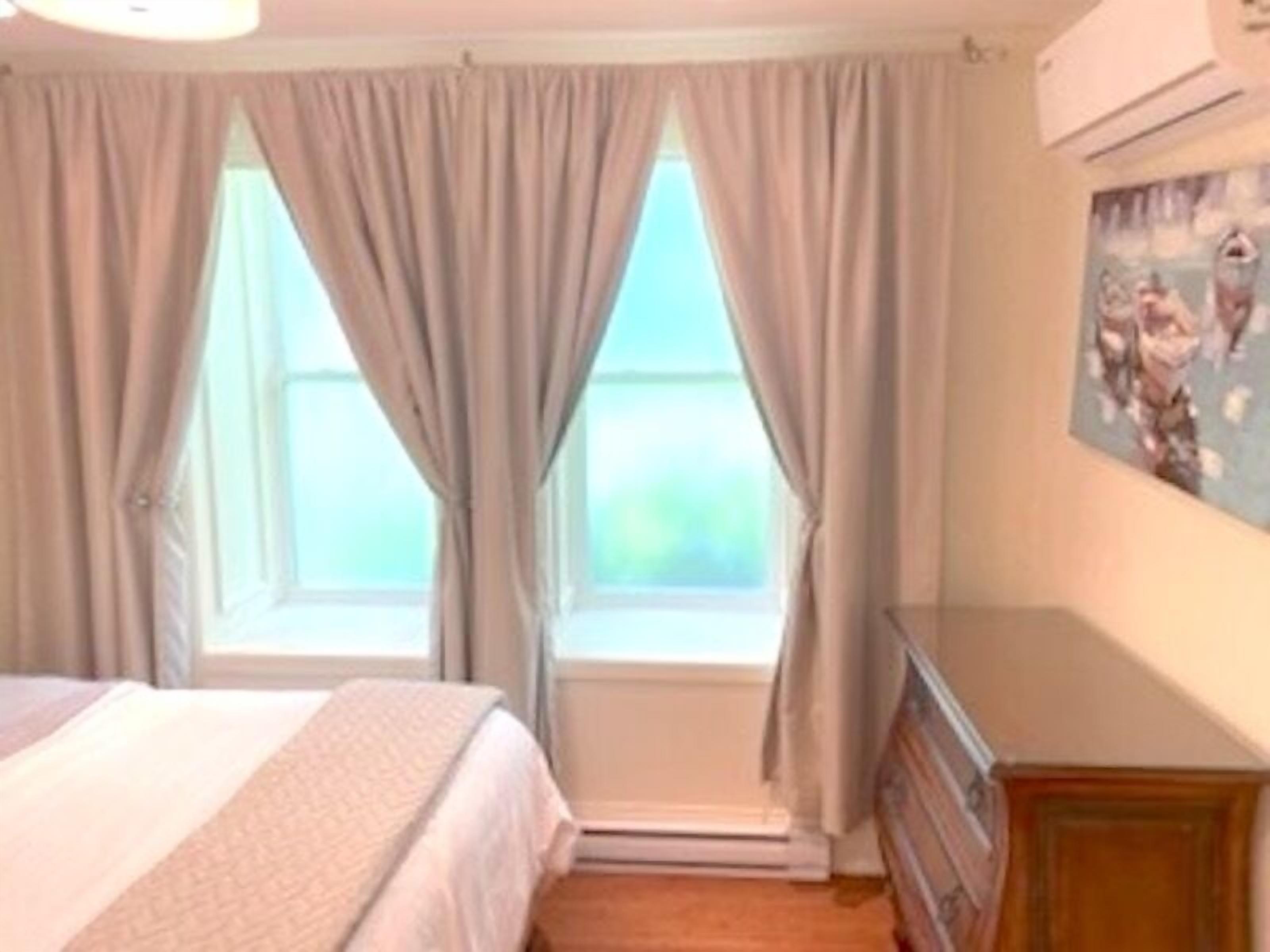 A bedroom with a bed, a dresser, and a window with curtains.