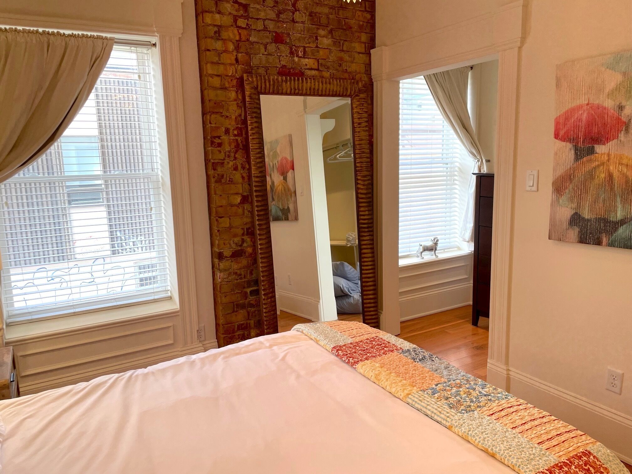 A bedroom with a large bed, a brick wall, a mirror, and a window with blinds.