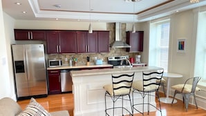 A modern kitchen with dark red cabinets, stainless steel appliances, and a central island with bar stools.