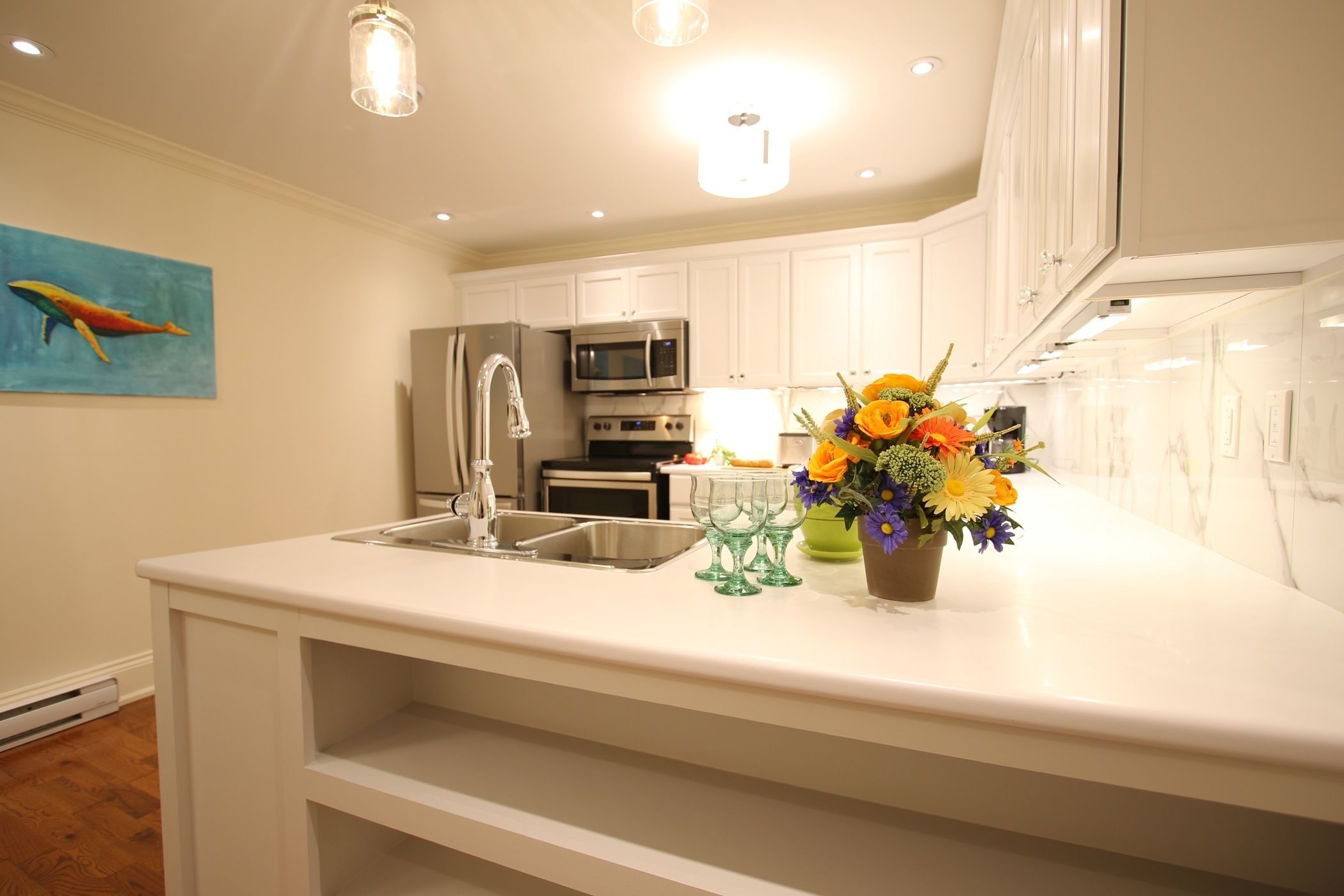 A modern kitchen with white cabinetry, stainless steel appliances, and a central island with a sink and a vase of flowers.