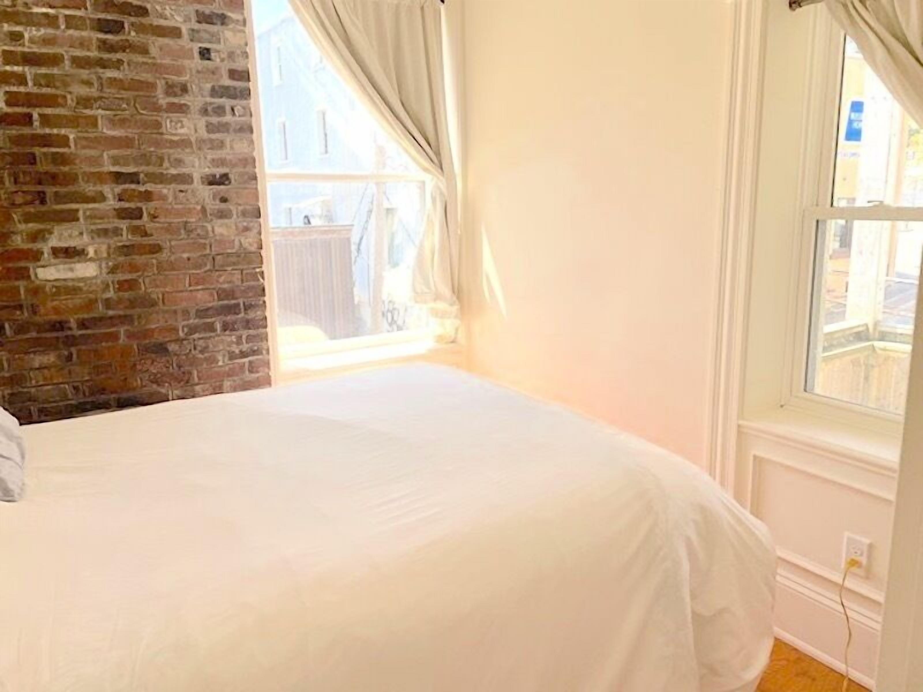 A bedroom with a brick wall, a large window, and a white bed.