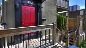 A building with a red door labeled "110 A" and a wooden balcony with a metal railing.