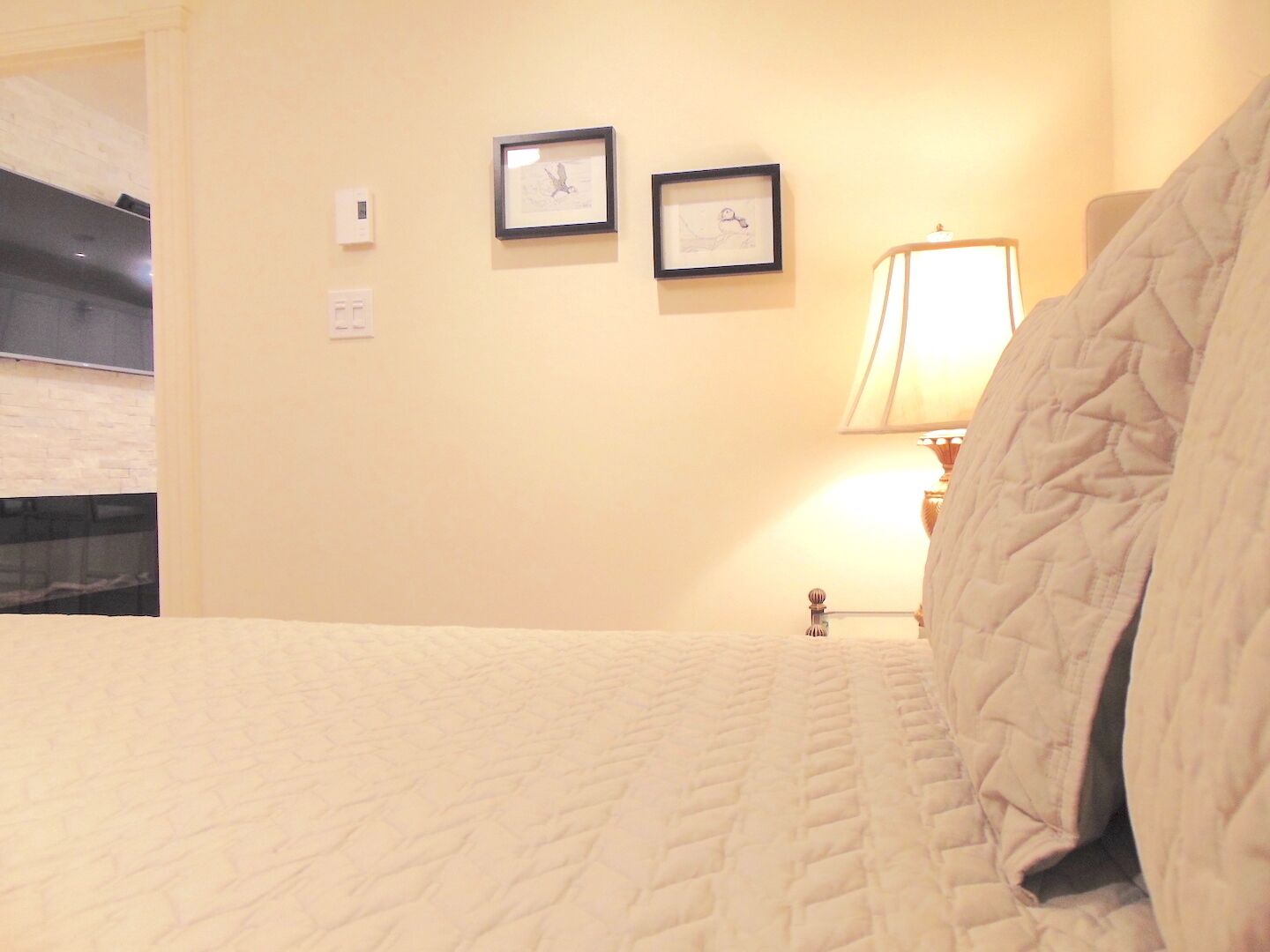Quarto de hotel com uma cama, uma luminária e duas imagens emolduradas na parede.