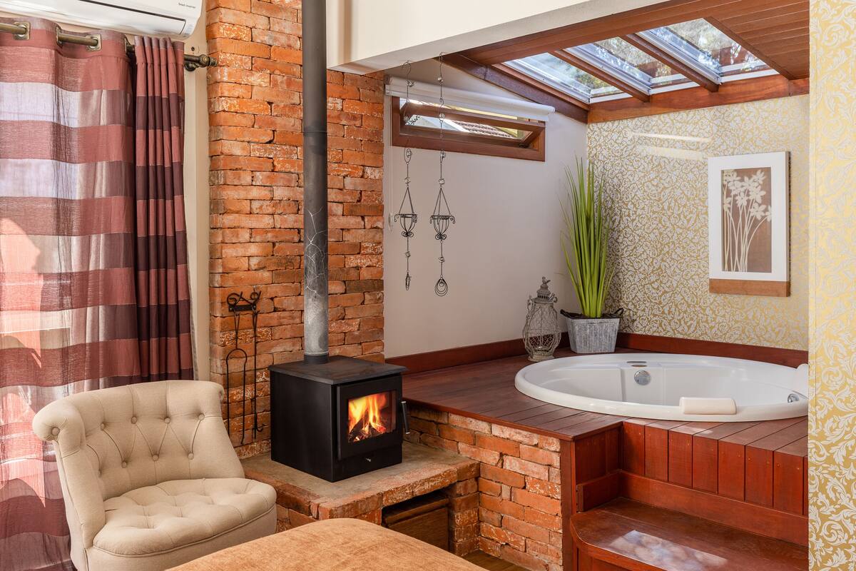A bathroom with a brick fireplace, a large bathtub, and a window above the sink.