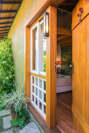 A wooden door leading to a room with a bed, a lamp, and a wall covered in greenery. - Pousada Jardim Secreto (Gramado)