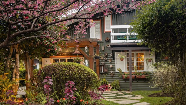 A garden with a stone pathway leading to a wooden structure with a bell. - Pousada Jardim Secreto (Gramado)