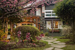 A garden with a stone pathway leading to a wooden structure with a bell. - Pousada Jardim Secreto (Gramado)