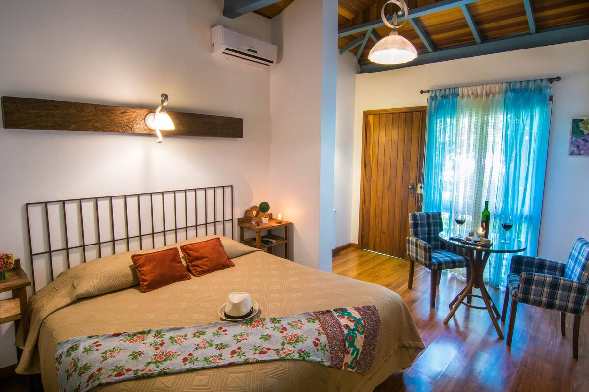 A bedroom with a large bed, a bedside table, a lamp, and a window with curtains.