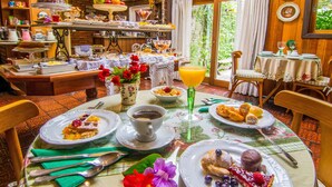 A breakfast setting with a table set for two, featuring plates of food, a coffee cup, and a fruit bowl. - Pousada Jardim Secreto (Gramado)