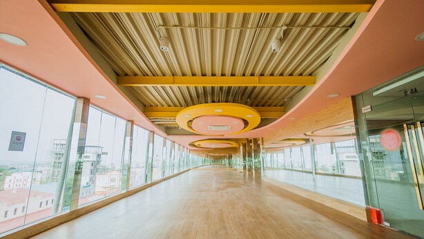A long, open hallway with a wooden floor and large windows on one side. - Green Rose Hotel (Batam)
