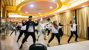 A dance class in a room with wooden floors and a high ceiling with yellow accents. - Green Rose Hotel (Batam)