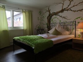 Uma cama com um cobertor verde, almofadas brancas e um mural de galho de árvore na parede.