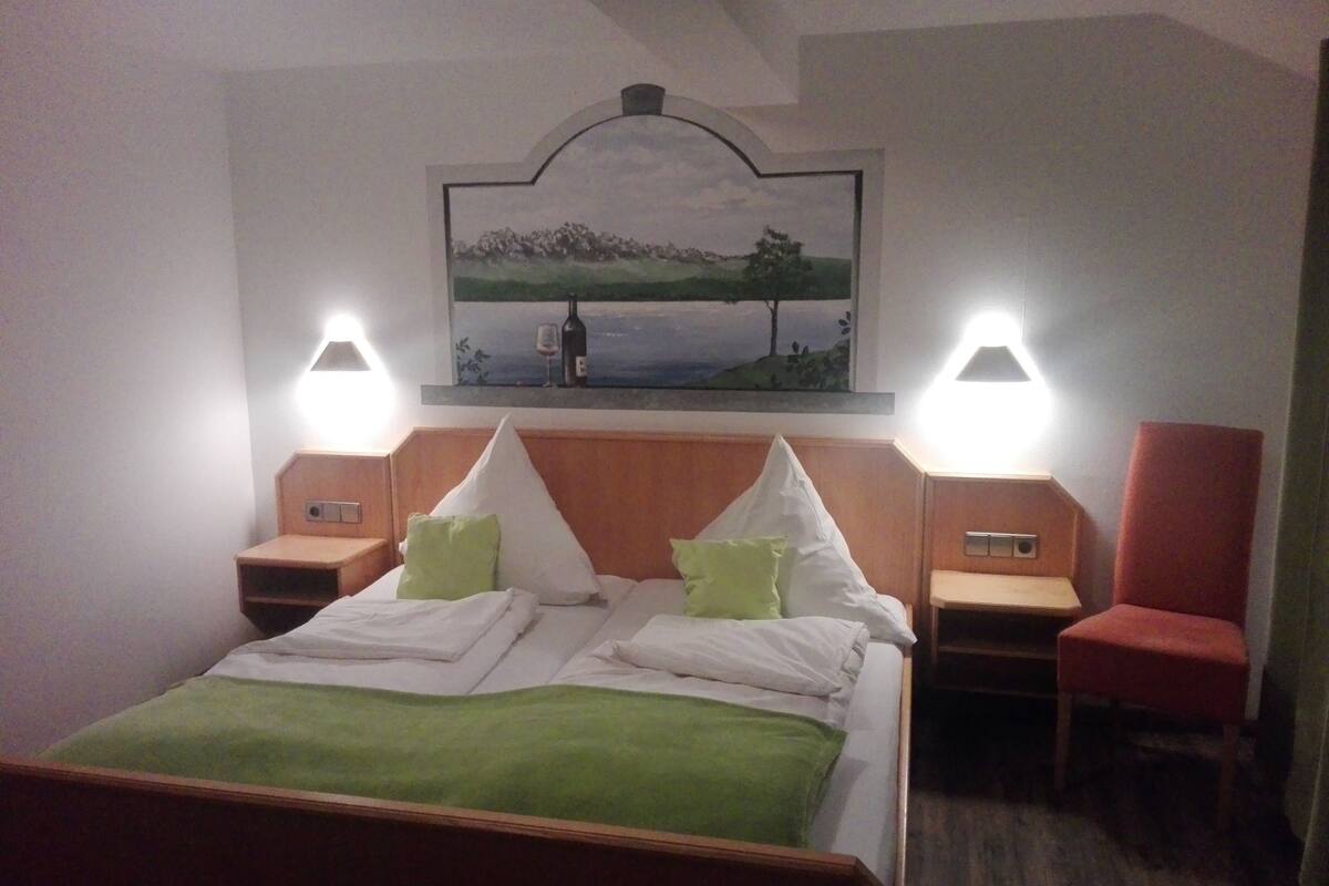 Habitación de hotel con una cama, dos mesitas de noche, una silla y un cuadro en la pared.