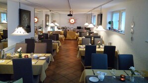 Een eetruimte met tafels gedekt voor maaltijden, hangende hanglampen en een zonvormige lamp aan de muur.