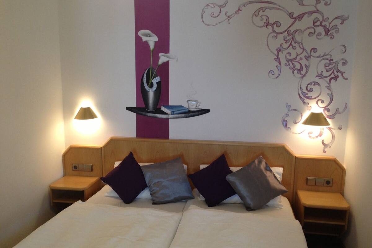 Habitación de hotel con cama, dos mesitas de noche y decoración en la pared.