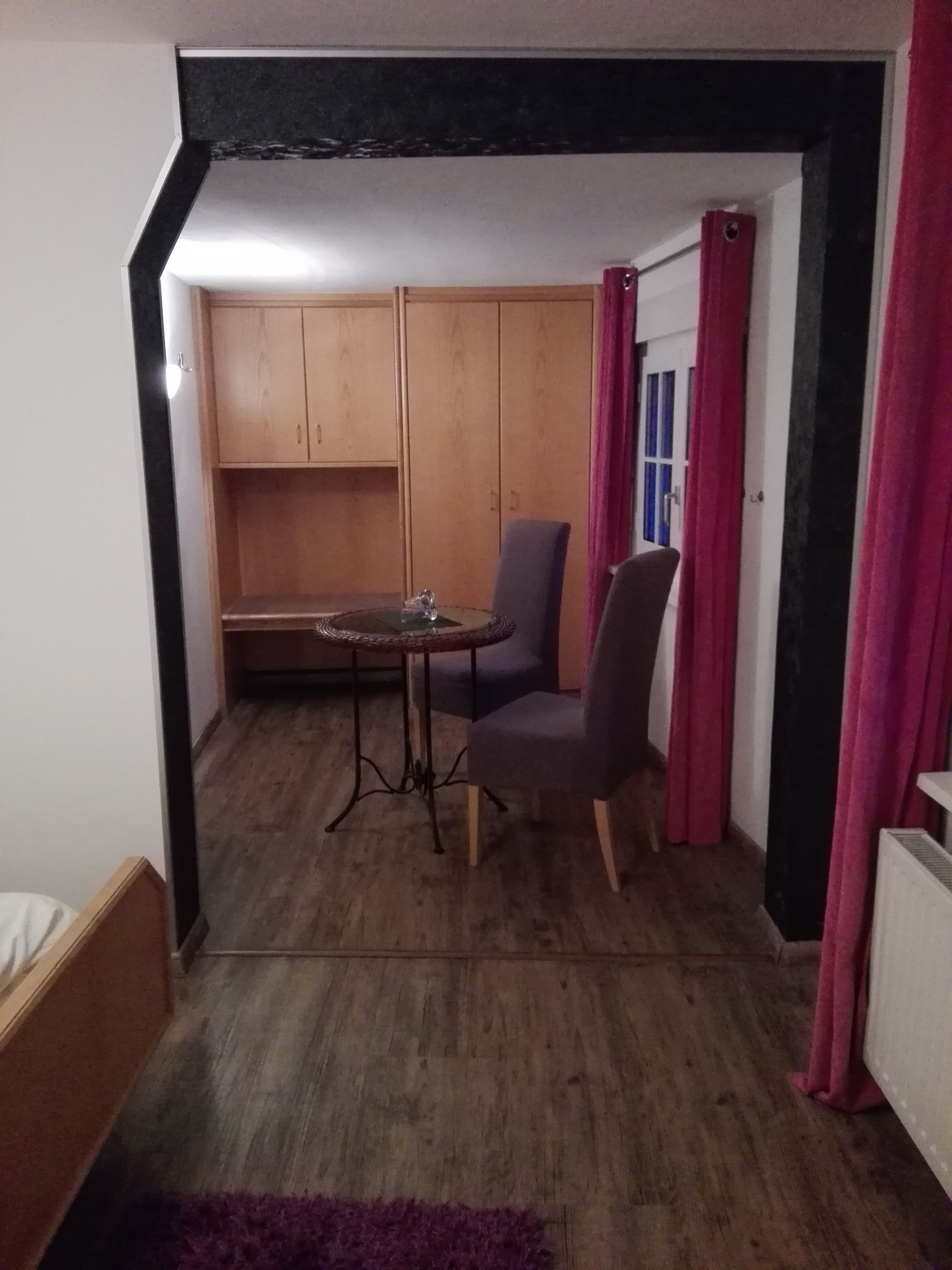 A small room with a wooden floor, a round table with a chair, a wardrobe, and a radiator.