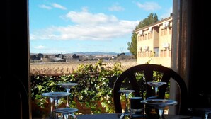 A table set with wine glasses and a coffee pot, overlooking a vineyard and a building. - Hotel-Motel Sol II (Requena)