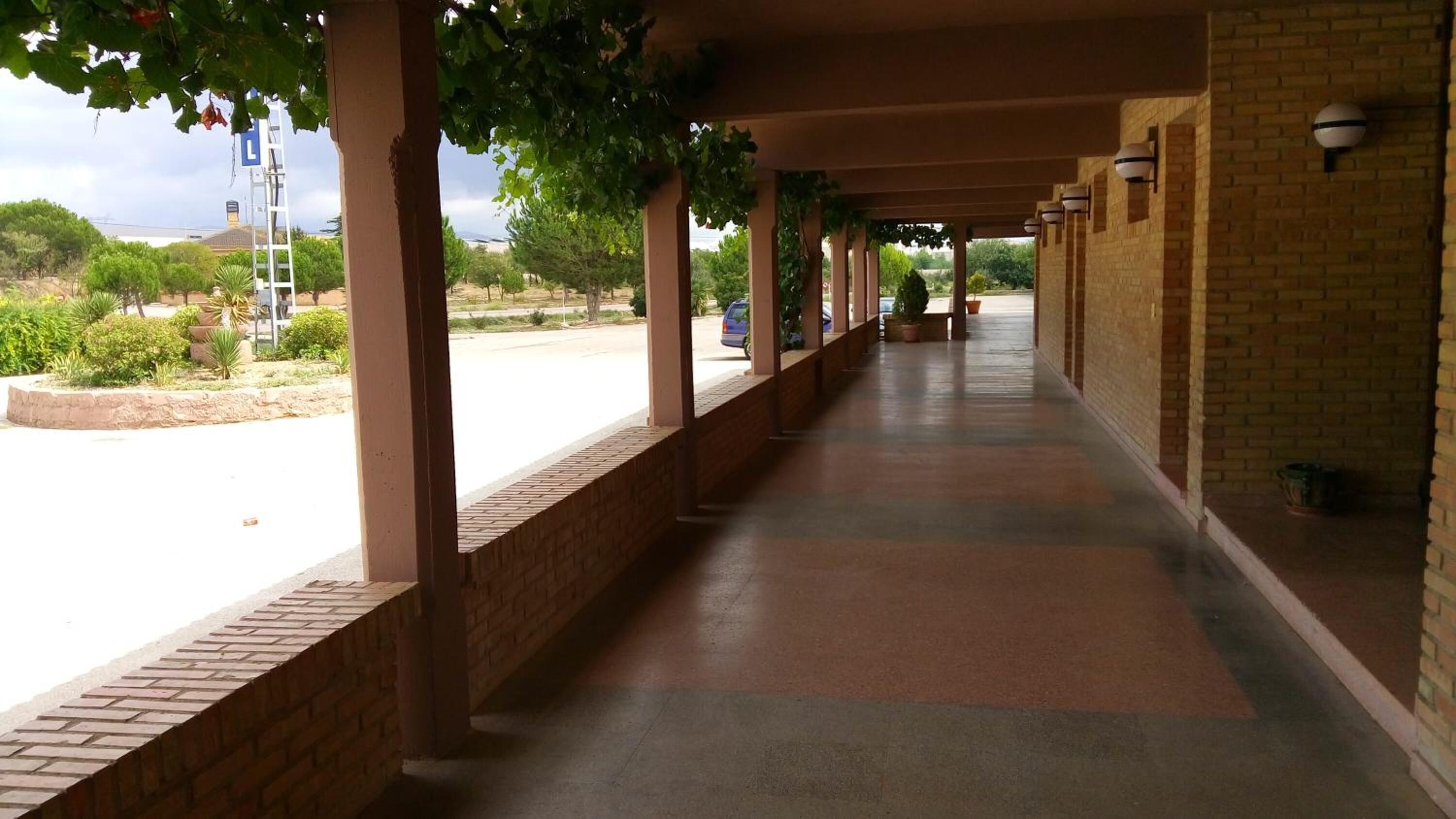 Un paseo techado con paredes de ladrillo y piso de baldosas, que conduce a un edificio con fachada de ladrillo.