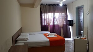 Habitació petita i senzilla amb llit, televisió penjada a la paret i finestra amb cortines.