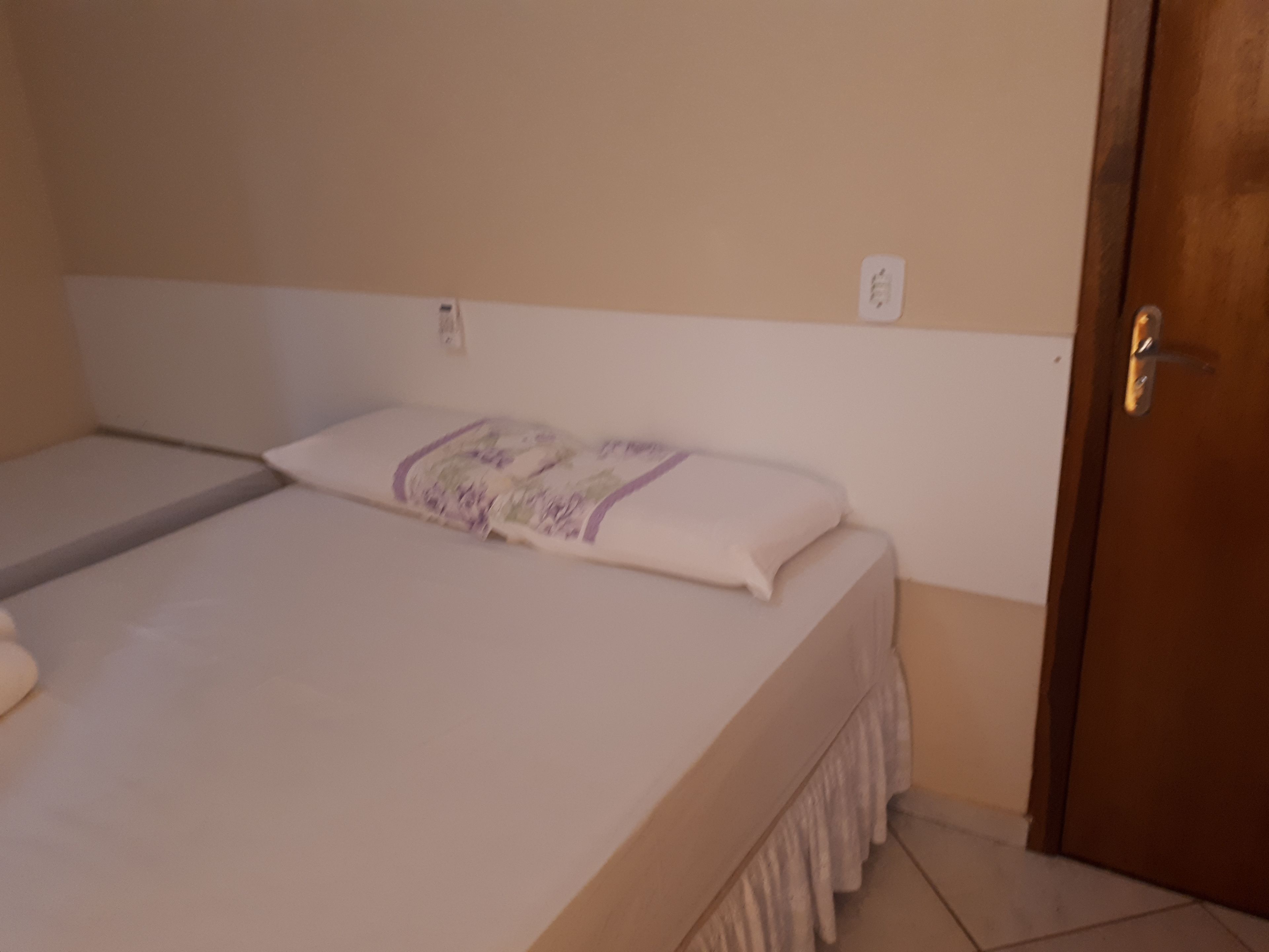 Uma cama de solteiro com colchão branco e manta roxa.