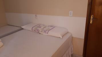 Uma cama de solteiro com colchão branco e manta roxa.