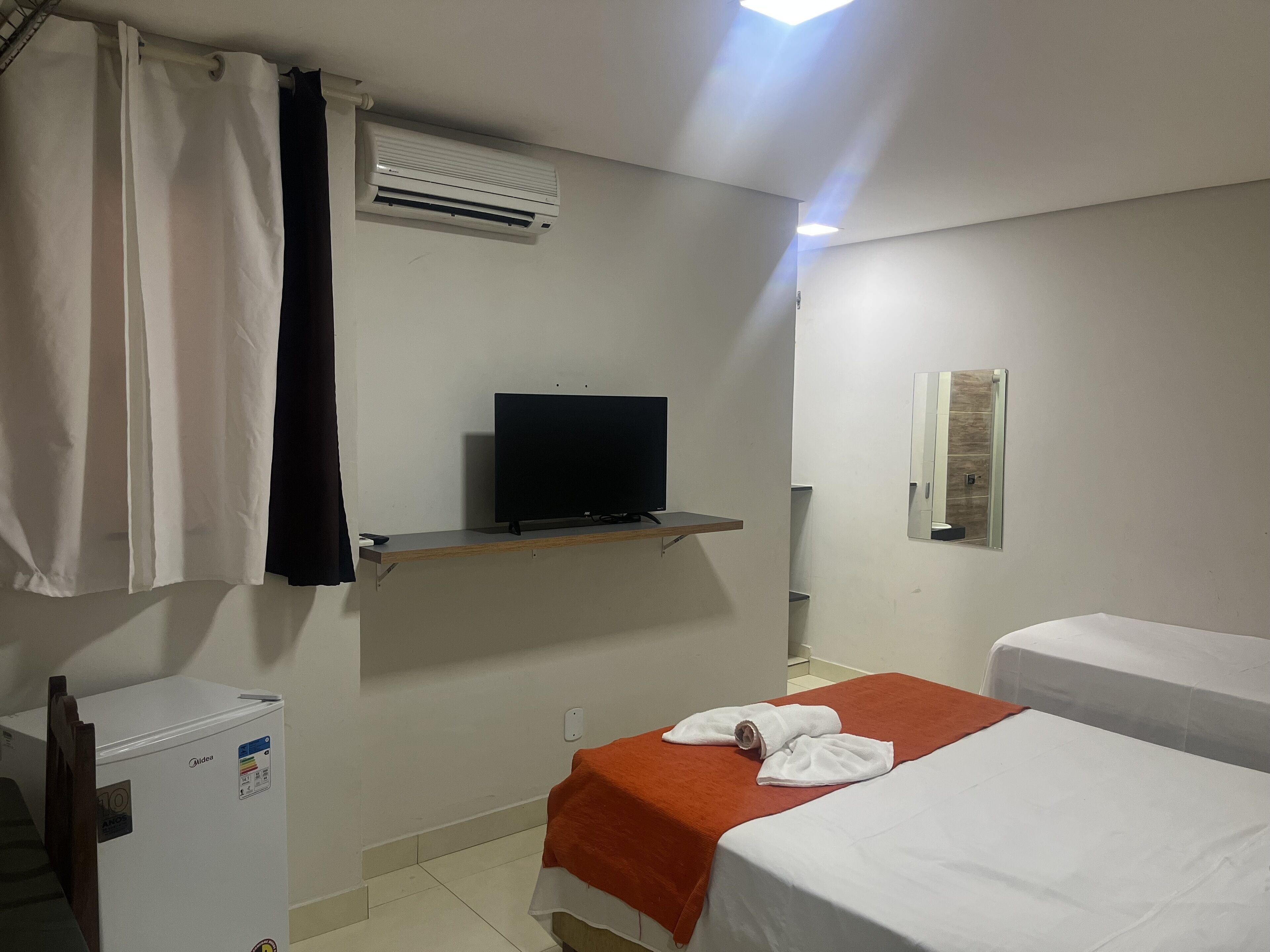 A hotel room with a bed, a TV on a shelf, a refrigerator, and a bathroom mirror.