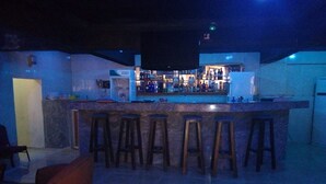 A bar area with a counter and stools, a seating area with a chair, and a visible bar sign. - New Gate Lodge & Hospitality Ltd (Abuja)