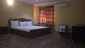 A hotel room with a bed, a desk, and an air conditioning unit. - New Gate Lodge & Hospitality Ltd (Abuja)