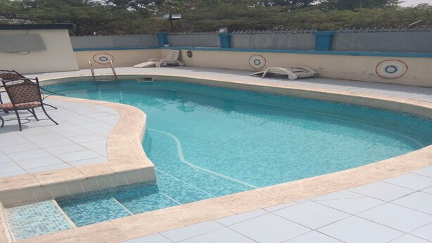 A swimming pool with tiled edges and a few lounge chairs. - New Gate Lodge & Hospitality Ltd (Abuja)
