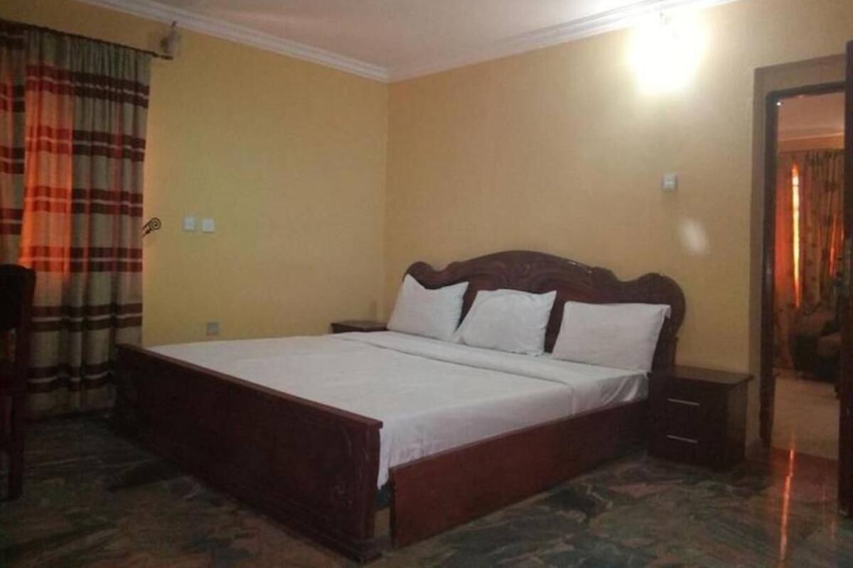 Un dormitorio con una cama de madera, una mesita de noche, una silla y una cortina.