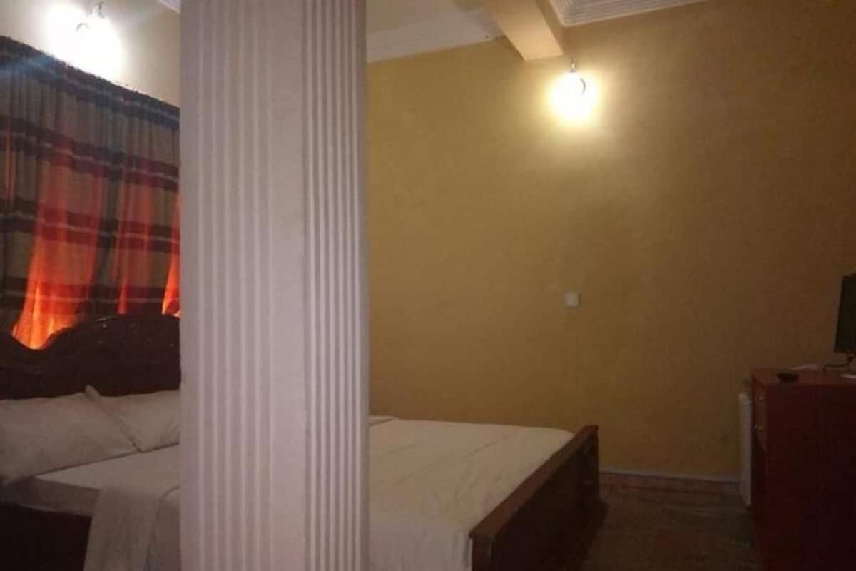 Una habitación con cama, mesita de noche, lámpara y cortina.