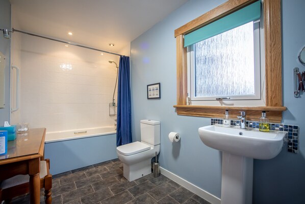 A bathroom with a bathtub, toilet, sink, and a window with a wooden frame.