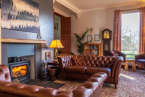 A cozy living room with a fireplace, leather furniture, and a bookshelf. - Crubenbeg Country House (Newtonmore)