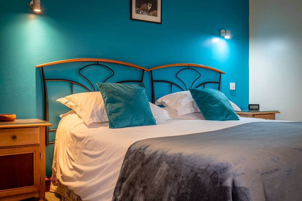 Un lit avec une tête de lit de couleur turquoise, des oreillers blancs et turquoise, et une couverture grise.