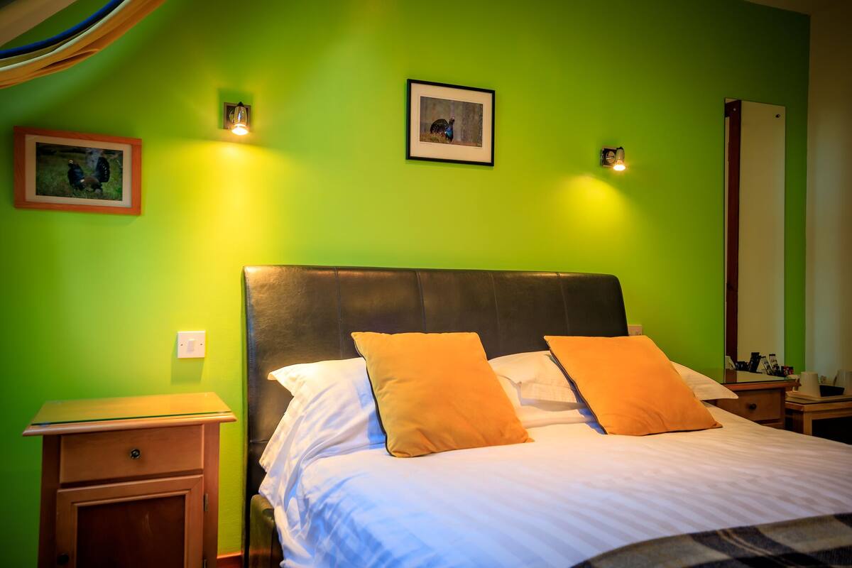 Une chambre d’hôtel comprenant un lit, deux oreillers, une table de chevet, un miroir et deux lampes fixées au mur.