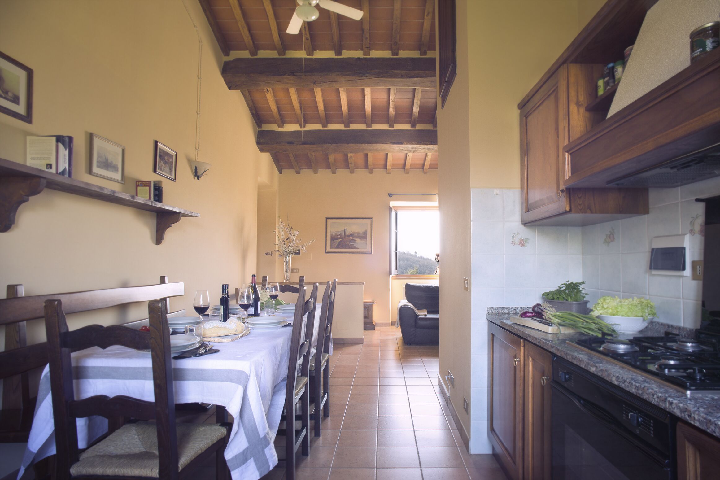 Un'area pranzo con un tavolo lungo apparecchiato per un pasto, sedie di legno e una ventola a soffitto.