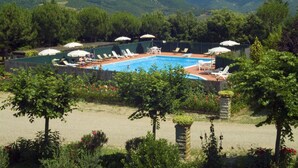 A pool area with lounge chairs and umbrellas, surrounded by greenery and hills in the background. - Buccia Nera (Arezzo)