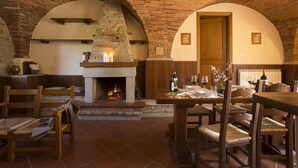 A rustic dining area with a brick fireplace, wooden furniture, and a stone wall. - Buccia Nera (Arezzo)
