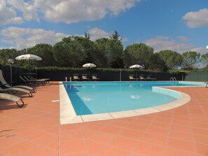 A swimming pool with sun loungers and umbrellas, surrounded by a tiled deck and trees. - Buccia Nera (Arezzo)