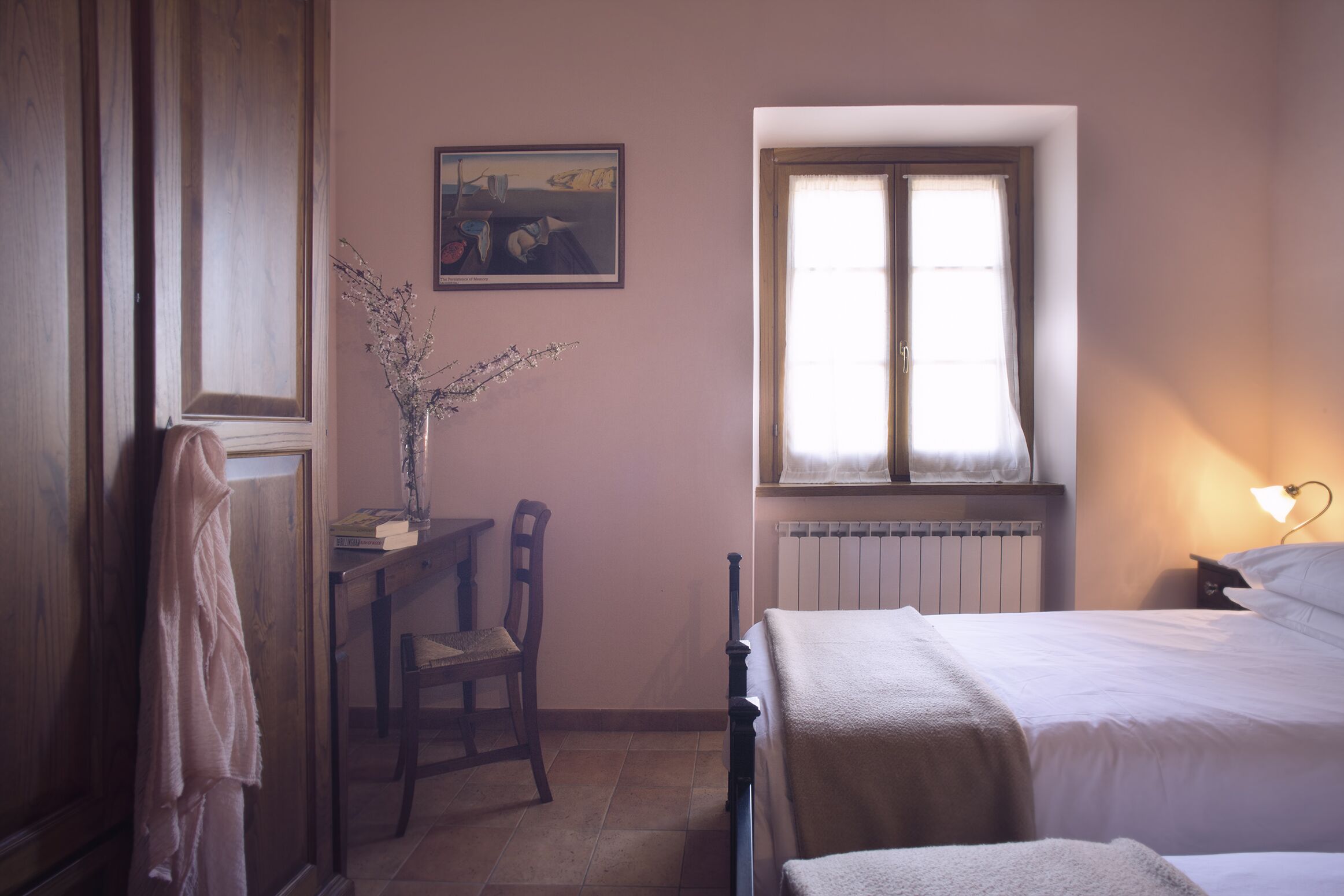 A bedroom with a bed, a chair, a desk, a window with curtains, and a radiator.
