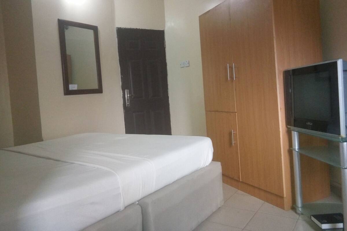 A bedroom with a bed, a wardrobe, a television, and a mirror.