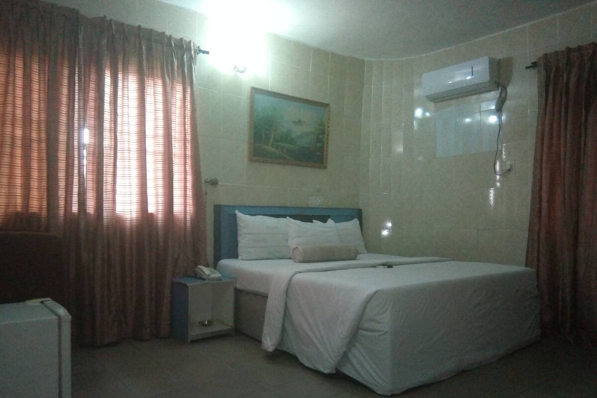 A hotel room with a bed, a nightstand, a telephone, and an air conditioning unit.